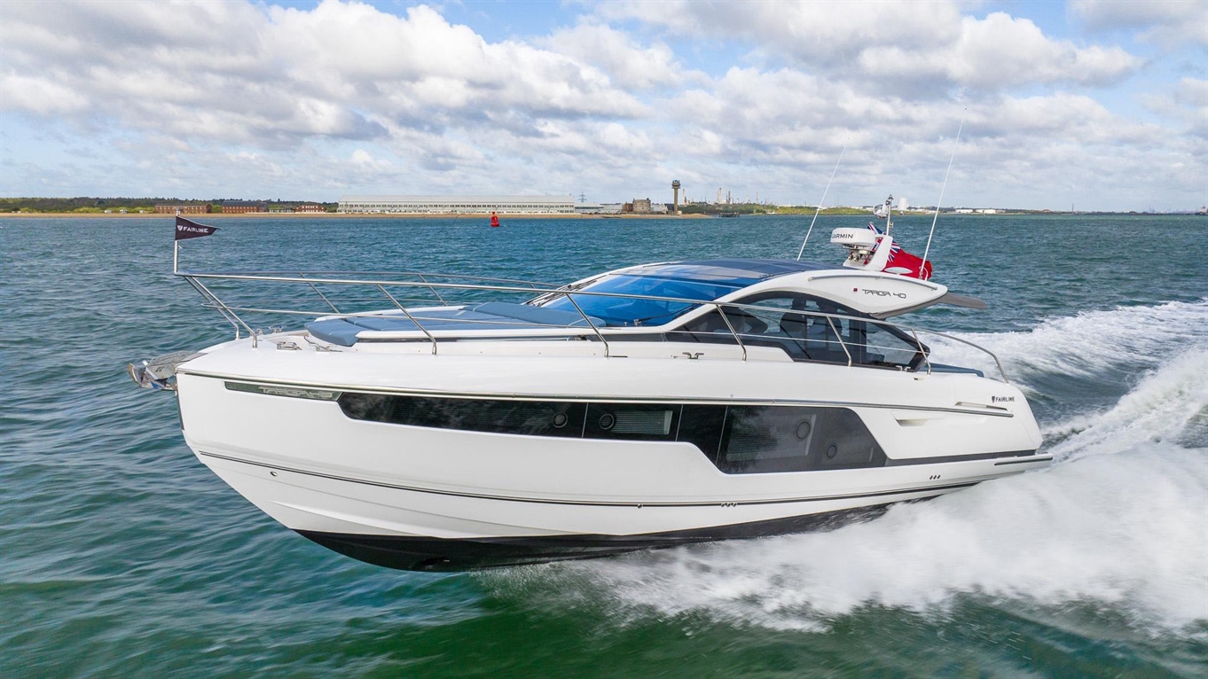 A sleek white motorboat glides quickly across the water, with a distant shoreline and blue sky in the background.
